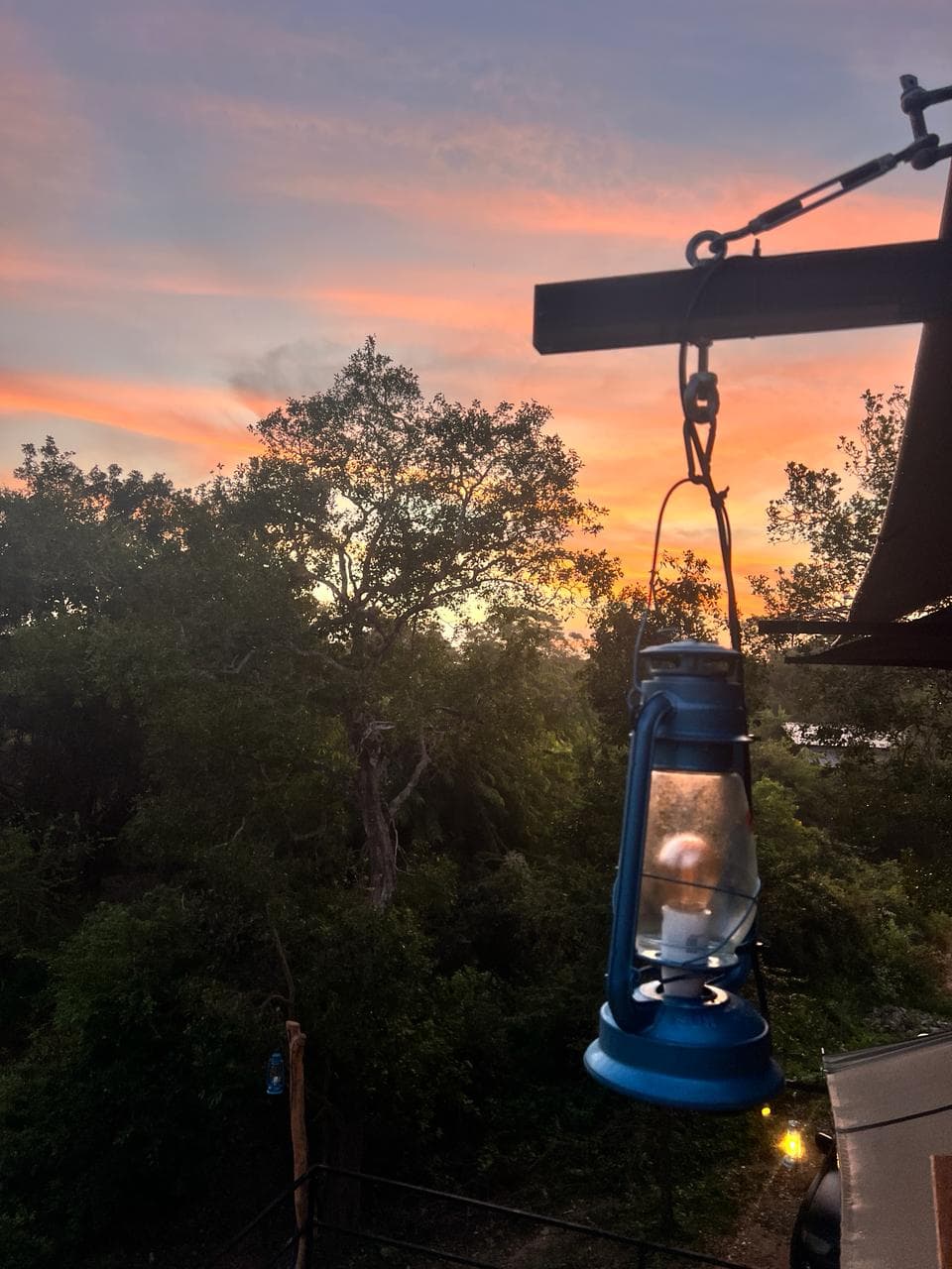 A hurricane lantern hanging from the roof beam against an orange sunset